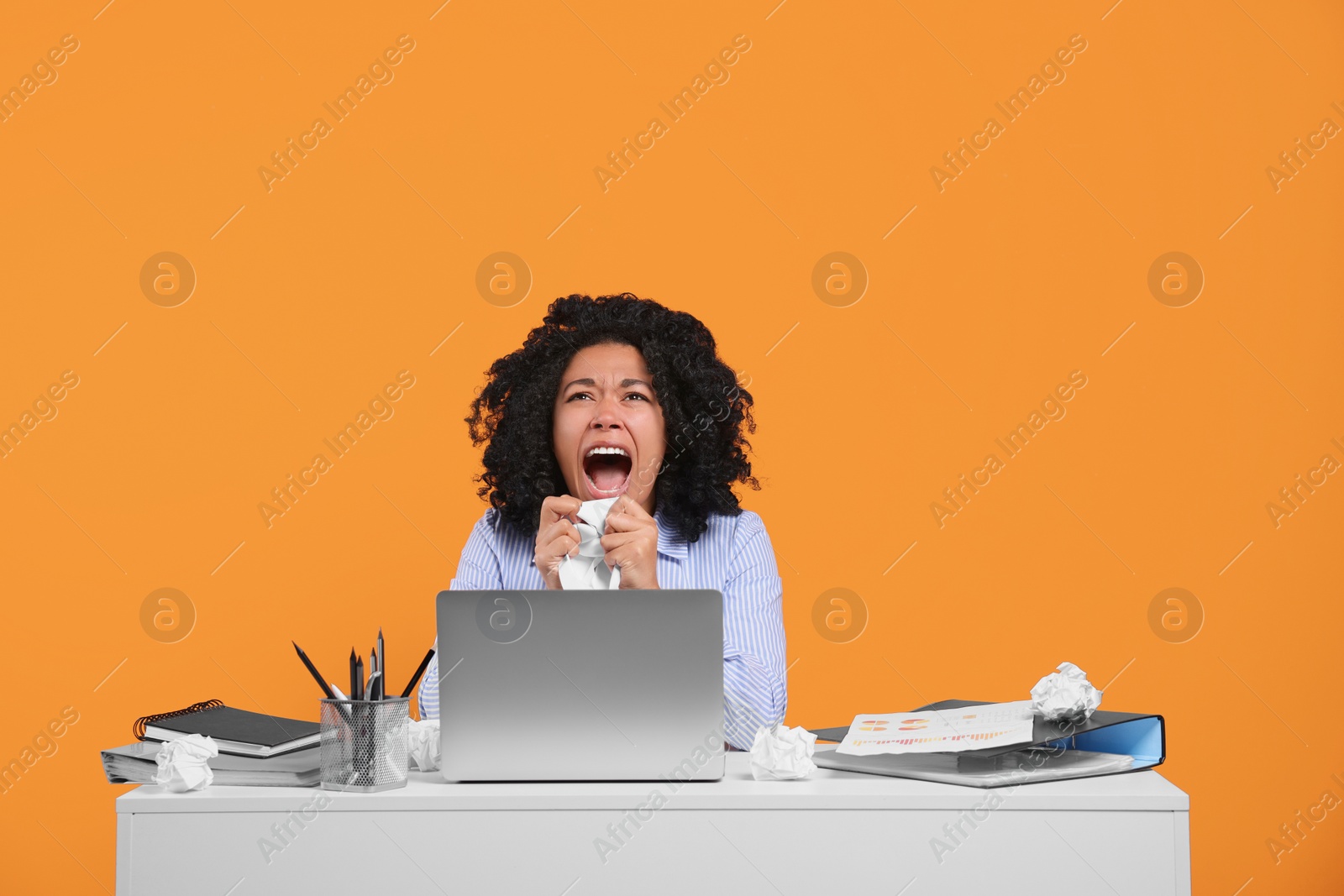 Photo of Stressful deadline. Screaming woman crumpling document at white desk against orange background