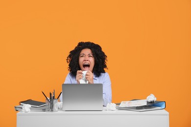 Stressful deadline. Screaming woman crumpling document at white desk against orange background