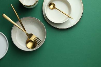 Photo of Stylish empty dishware and golden cutlery on green background, flat lay. Space for text