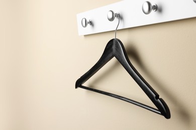 Photo of Rack with empty black clothes hanger on beige wall. Space for text