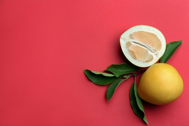 Photo of Fresh cut and whole pomelo fruits with leaves on red background, flat lay. Space for text