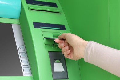 Woman inserting credit card into green cash machine, closeup