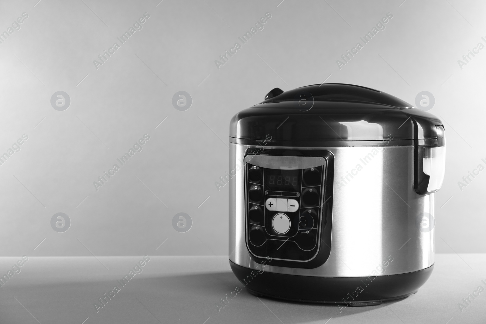 Photo of Modern powerful multi cooker on table against grey background. Space for text