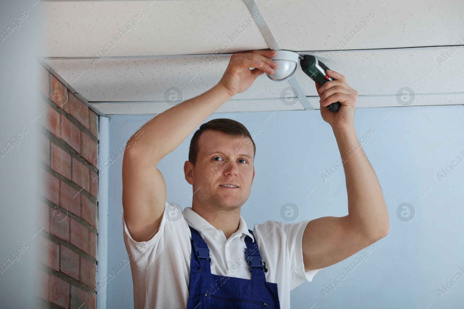 Photo of Technician installing CCTV camera on ceiling indoors