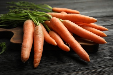 Photo of Board with ripe carrots on wooden background