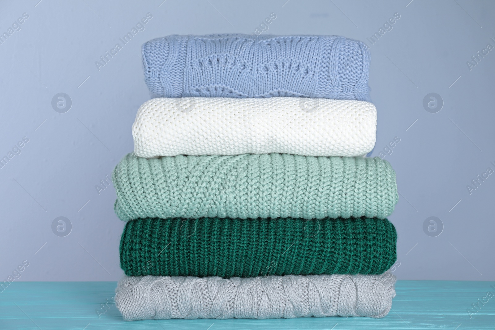 Photo of Stack of folded knitted sweaters on blue wooden table against grey background