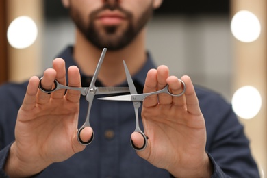 Photo of Hairstylist holding professional scissors in beauty salon, closeup