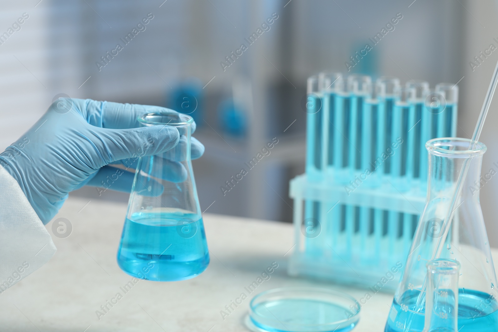 Photo of Scientist with beaker of light blue liquid in laboratory, closeup