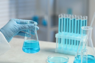 Scientist with beaker of light blue liquid in laboratory, closeup
