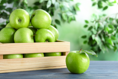 Ripe green apples in crate on blue wooden table against blurred background. Space for text