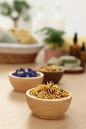 Photo of Bowls of dry flowers on light wooden table. Spa therapy