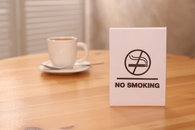 Photo of No Smoking sign and cup of drink on wooden table indoors, selective focus