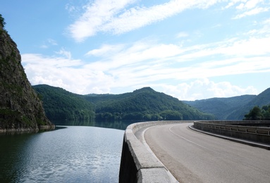 Image of Beautiful lake near hills covered with green forest. View from road