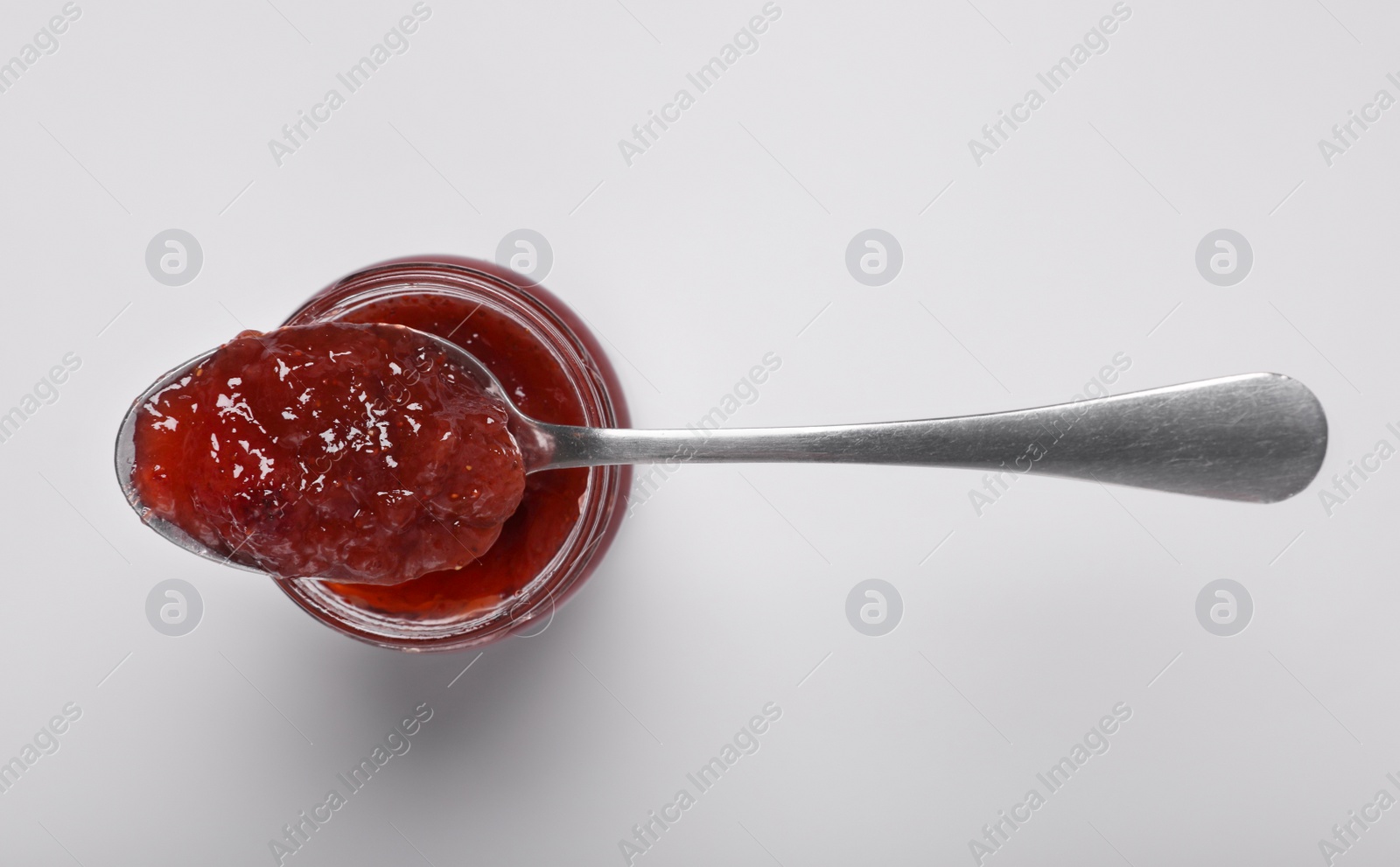 Photo of Spoon with tasty canned raspberry jam on jar against white background, top view