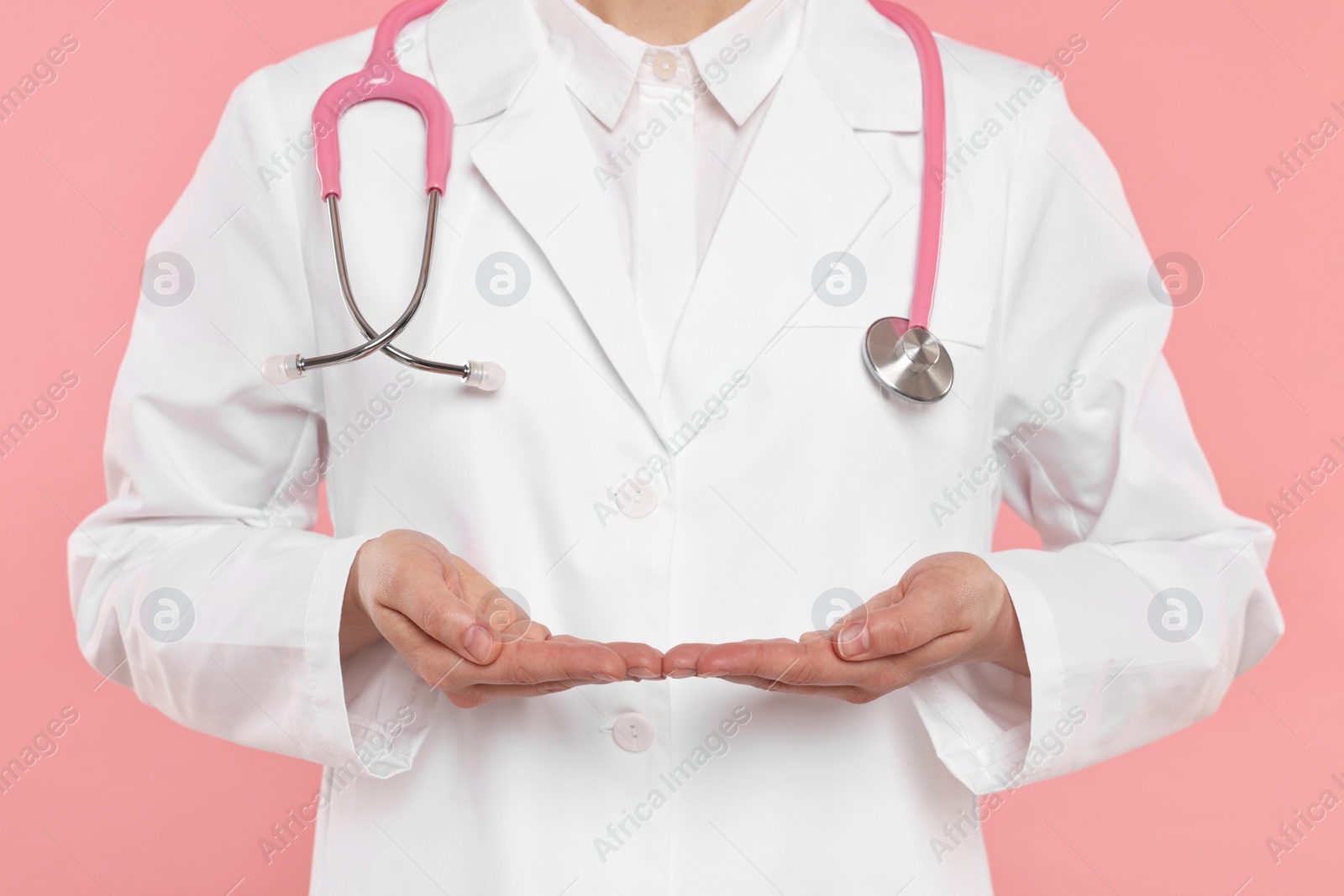 Photo of Doctor with stethoscope holding something on pink background, closeup