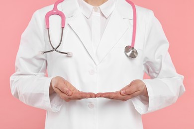 Doctor with stethoscope holding something on pink background, closeup