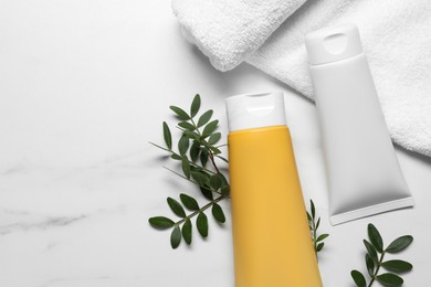 Photo of Tubes of face cleansing products, towel and green leaves on white marble table, flat lay. Space for text