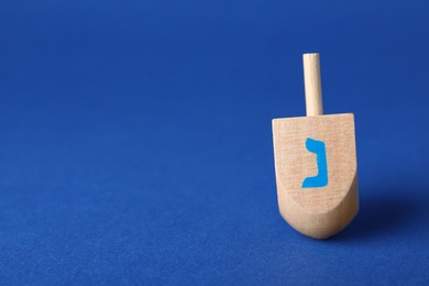 Photo of Hanukkah traditional dreidel with letter Nun on blue background, space for text