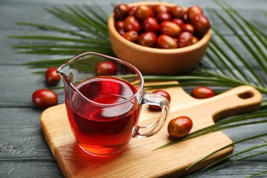 Palm oil in glass jug, tropical leaf and fruits on grey wooden table