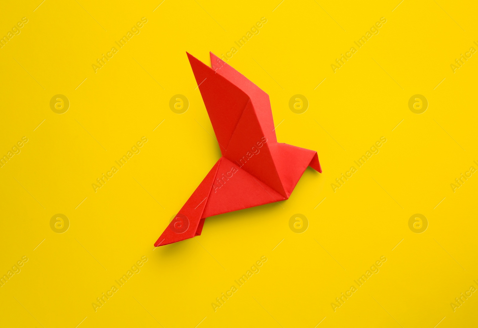 Photo of Origami art. Beautiful handmade paper bird on yellow background, top view