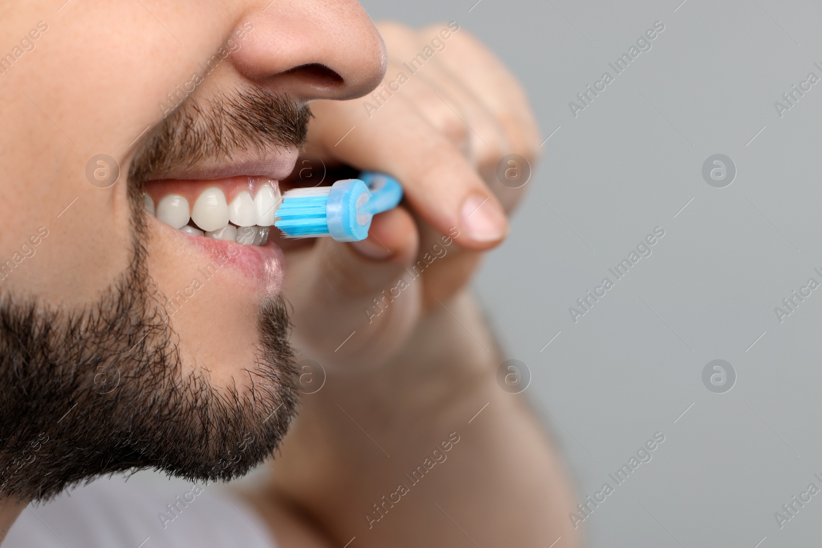 Photo of Man brushing his teeth with plastic toothbrush on light grey background, closeup. Space for text