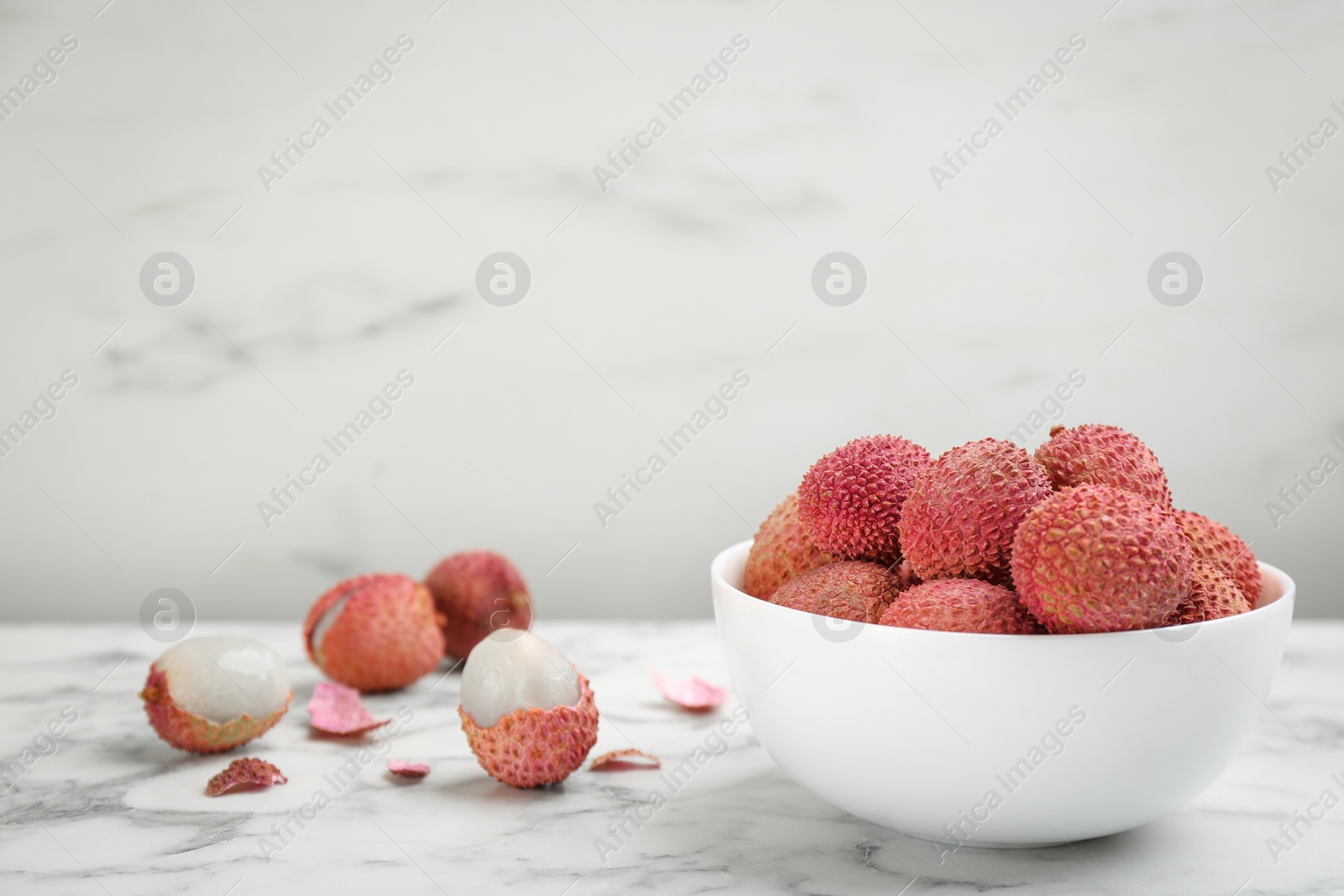 Photo of Fresh ripe lychee fruits in ceramic bowl on white marble table. Space for text