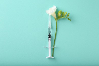 Photo of Cosmetology. Medical syringe and freesia flower on turquoise background, top view