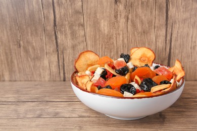 Bowl with different tasty dried fruits on wooden table. Space for text