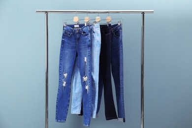 Photo of Rack with stylish jeans on color background