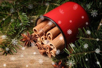 Cinnamon in red mug and anise surrounded by fir tree branches on wooden table, closeup