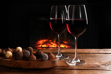 Photo of Red wine and chocolate truffles on wooden table against fireplace