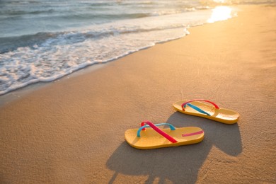 Bright yellow beach slippers on sand near sea, space for text