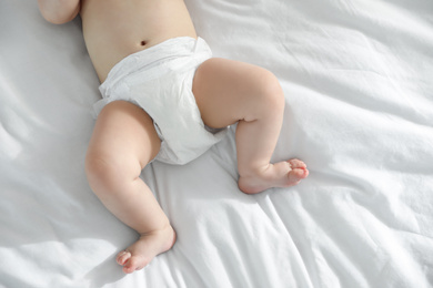 Photo of Little baby in diaper lying on bed at home, closeup view