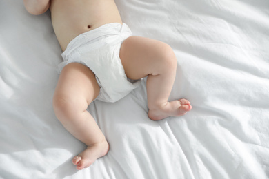 Little baby in diaper lying on bed at home, closeup view