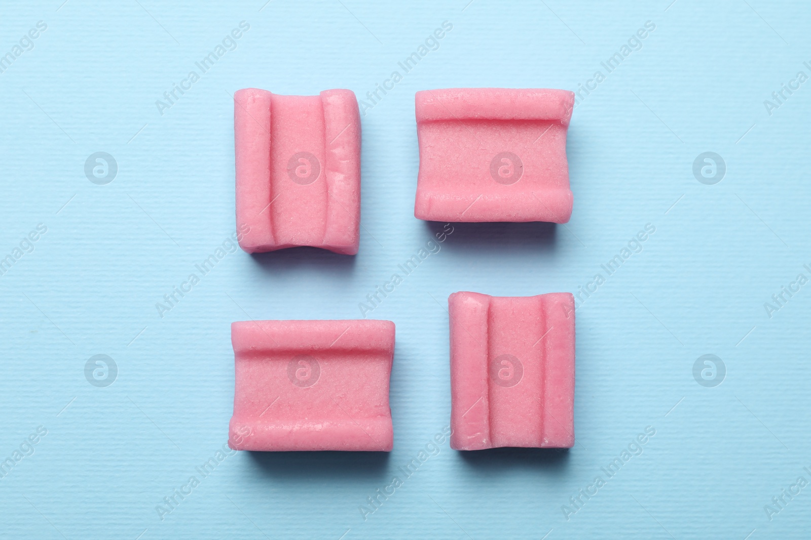 Photo of Tasty pink chewing gums on light blue background, flat lay