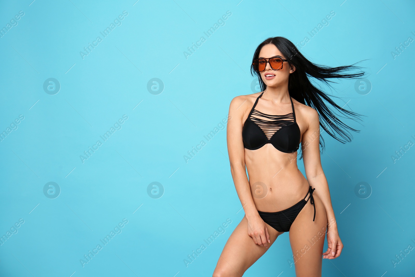 Photo of Beautiful young woman in stylish bikini with sunglasses on light blue background. Space for text