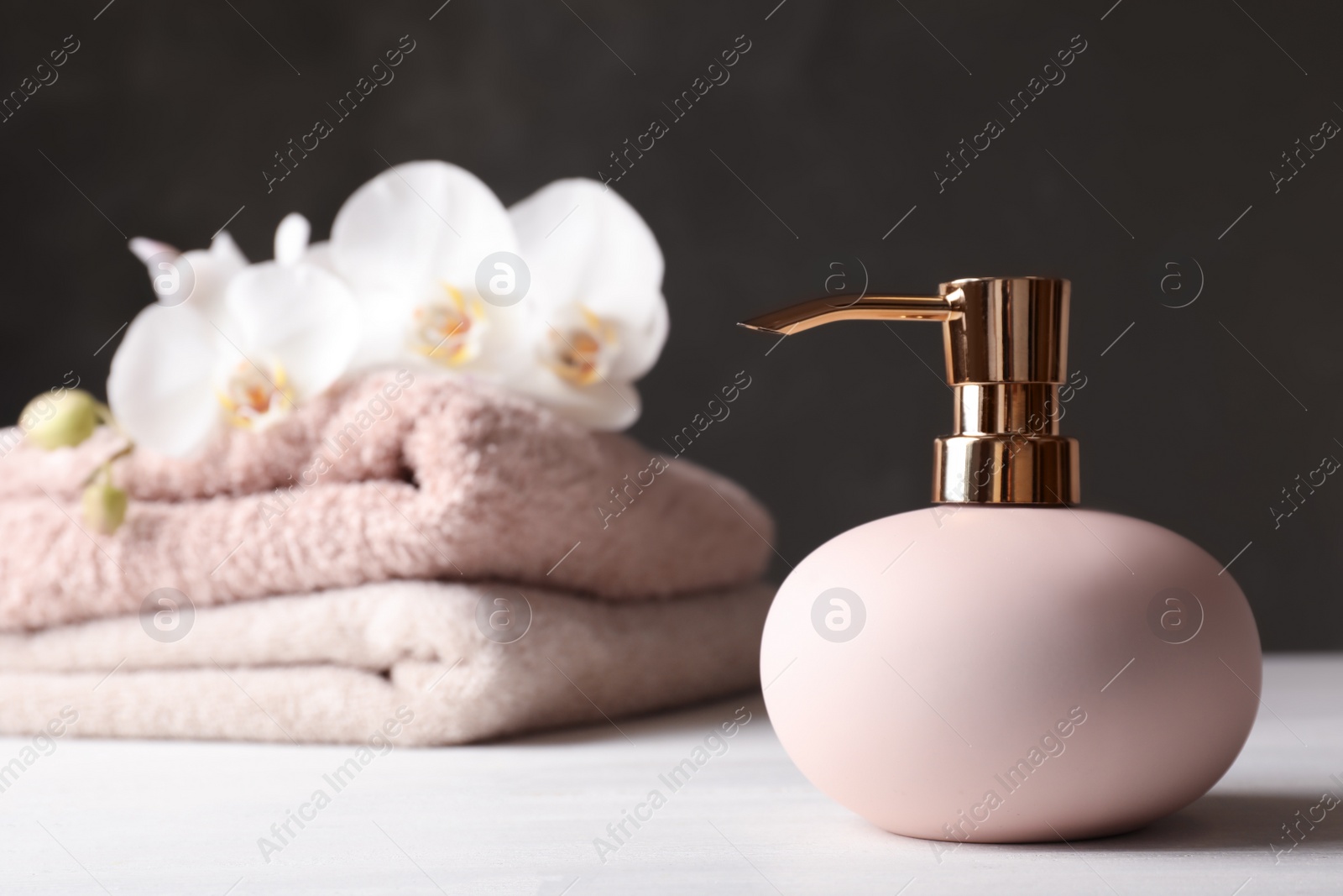 Photo of Stylish soap dispenser and towels with flowers on table. Space for text