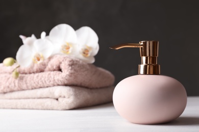 Stylish soap dispenser and towels with flowers on table. Space for text