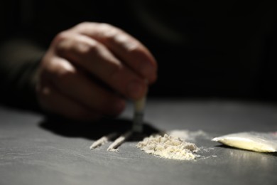 Photo of Addicted man with hard drug and rolled dollar banknote preparing for consumption at grey table, selective focus