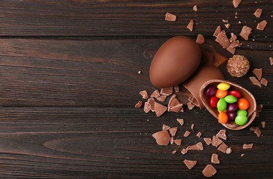 Photo of Broken and whole chocolate eggs with sweets on wooden table, flat lay. Space for text