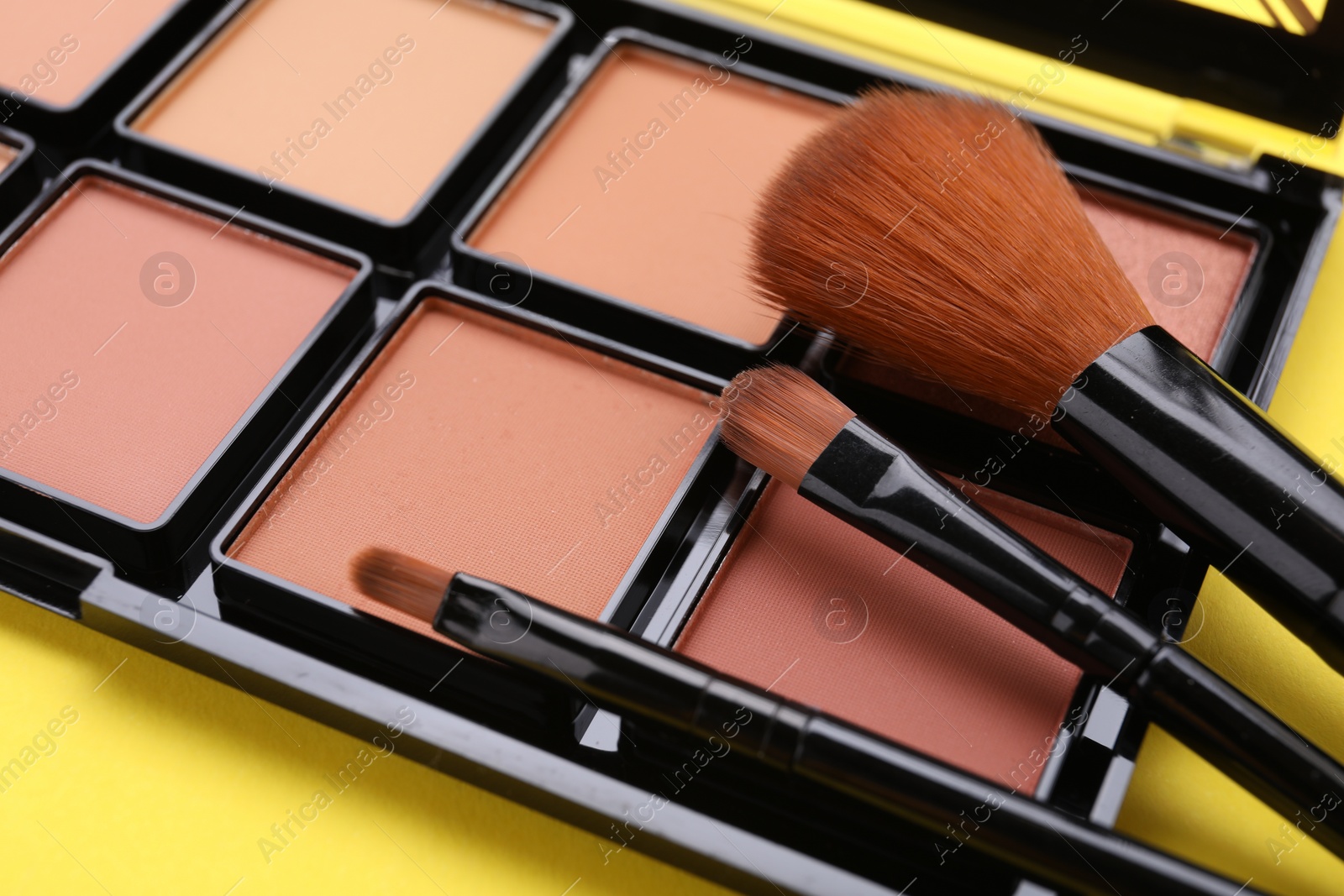 Photo of Colorful contouring palette with brushes on yellow background, closeup. Professional cosmetic product