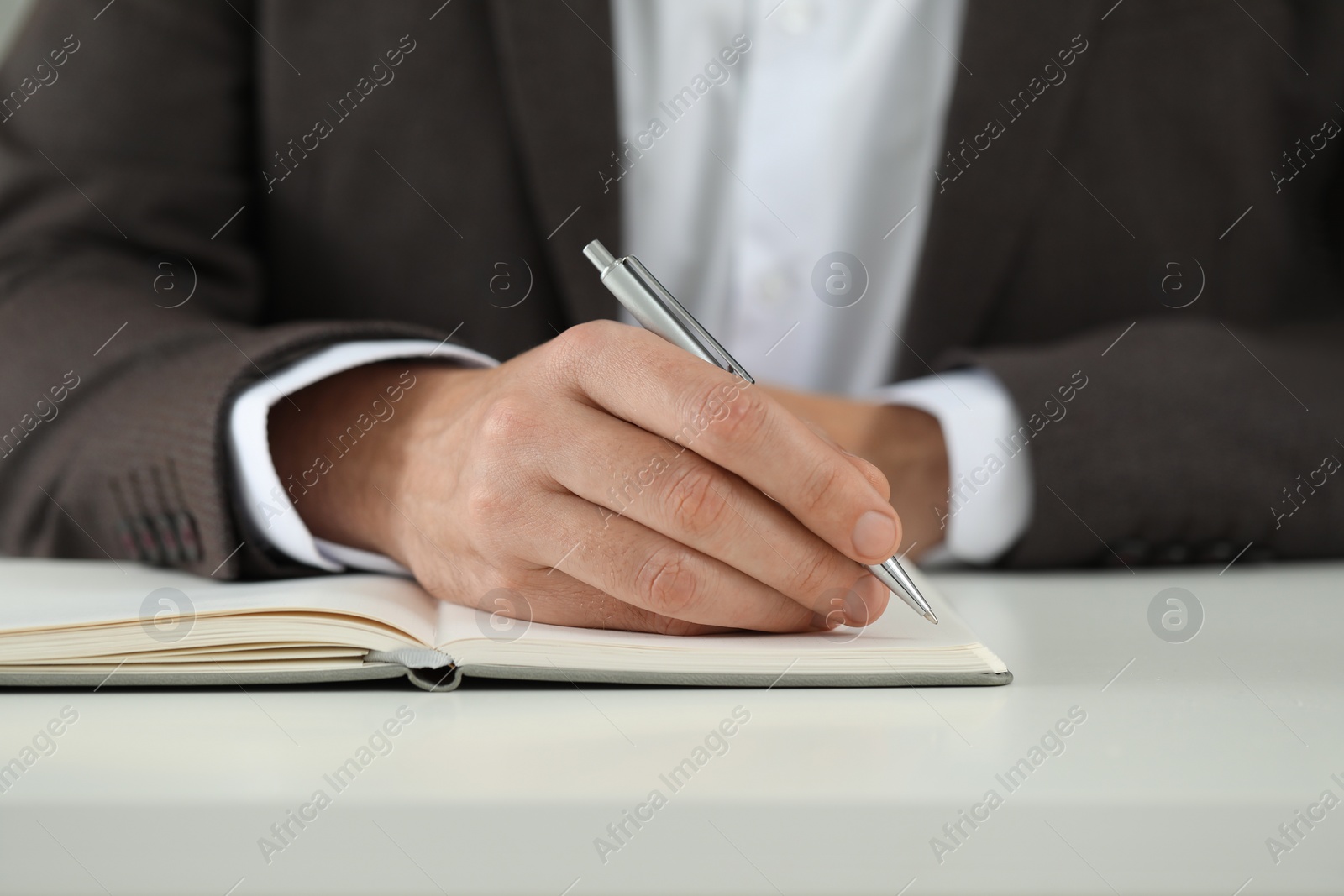 Photo of Man writing in notebook at white table, closeup