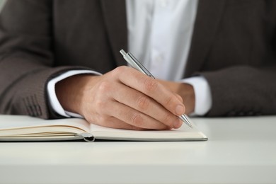 Man writing in notebook at white table, closeup