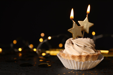 Birthday cupcake with candles on table against black background, space for text