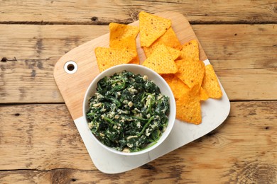 Photo of Tasty spinach dip with eggs in bowl and nachos chips on wooden table, top view