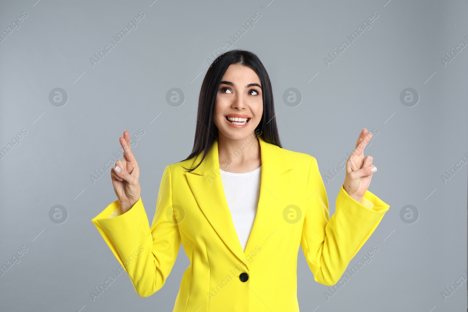 Photo of Woman with crossed fingers on grey background. Superstition concept