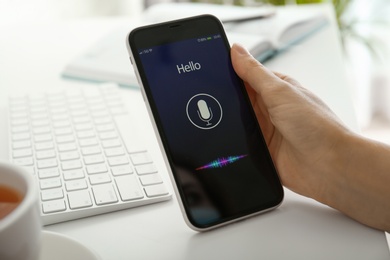 Photo of Woman using voice search on smartphone at white table, closeup