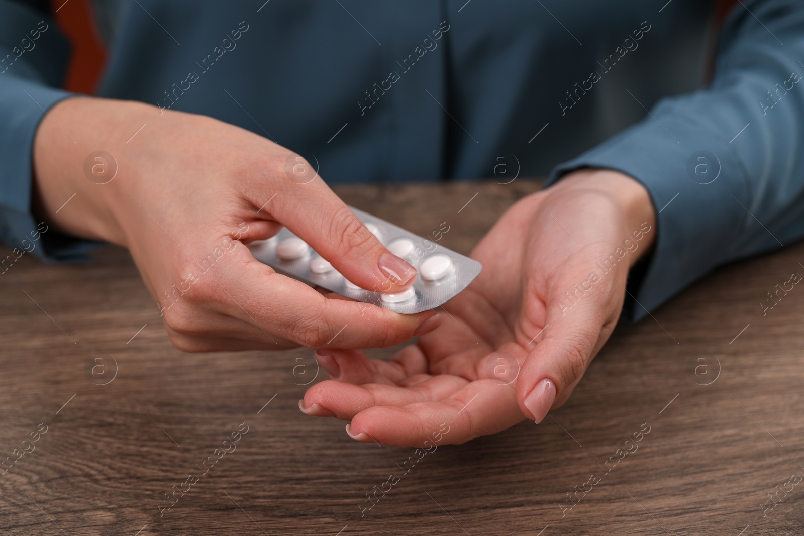 Photo of Woman taking antidepressant pill out from blister at wooden table, closeup