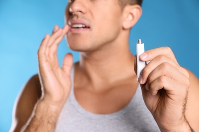 Man with herpes applying cream on lips against light blue background, closeup