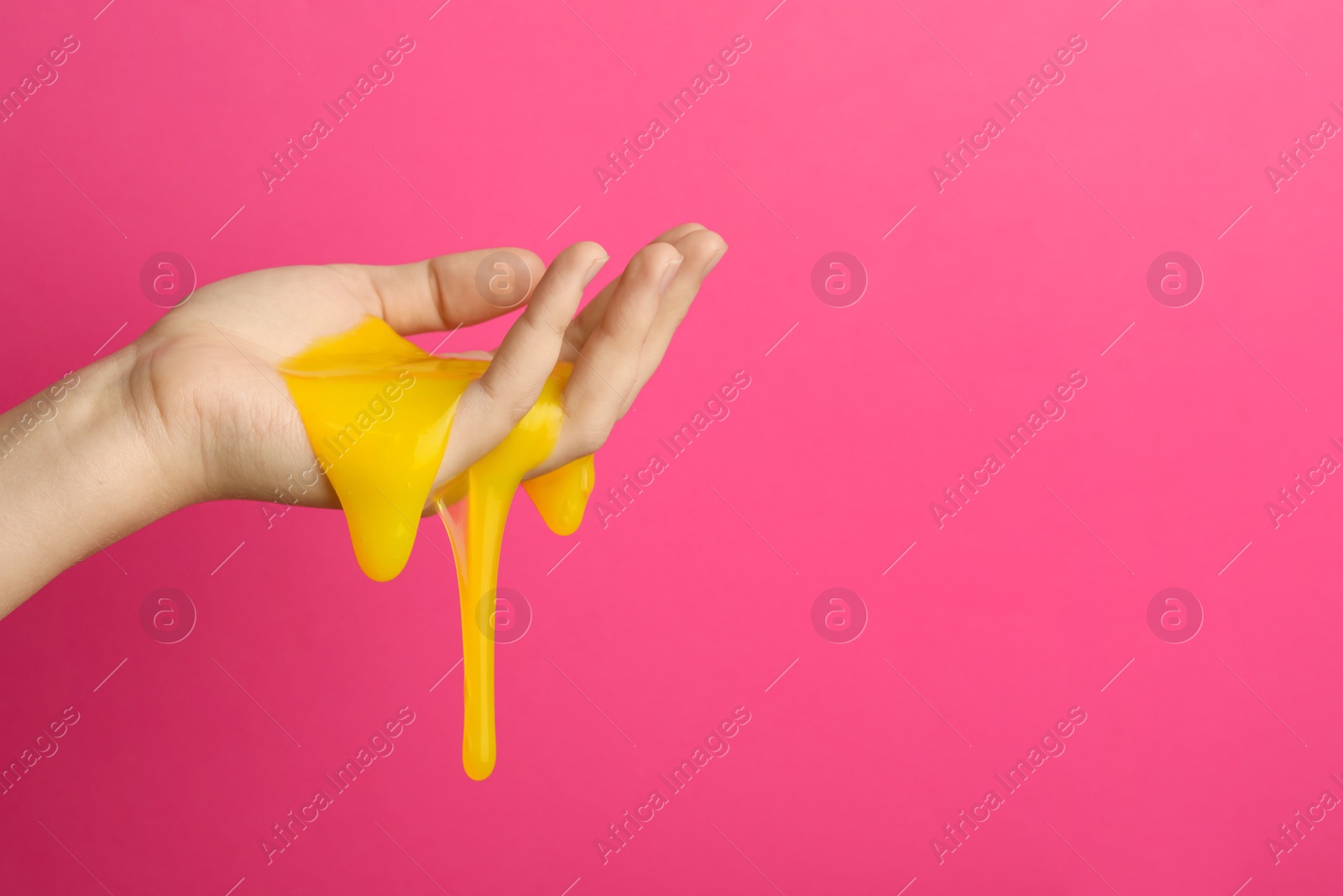 Photo of Woman playing with yellow slime on pink background, closeup. Antistress toy